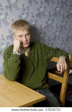 young handsome thoughtful blond man is sitting  at the wall
