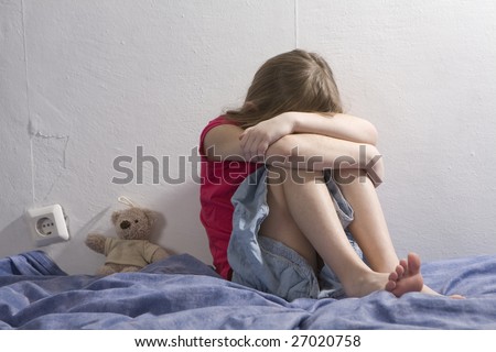 little upset girl sitting on the bed hugging her knees