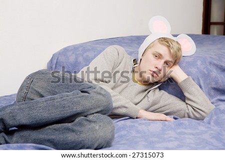 young blond handsome thoughtful man in funny cap lying on the bed. Teen`s life. Sad birthday