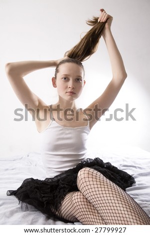 young attractive serious girl doing hair up sitting on bed. Morning