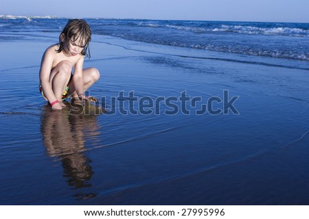 Little cute girl five years old playing in sand on shore in sunset