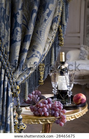 Curtain and bottle of vine with grape standing on table