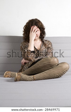 Young attractive woman wearing leopard blouse  close eyes by hands sitting on sofa with legs in shoes. Woman`s problem. White background