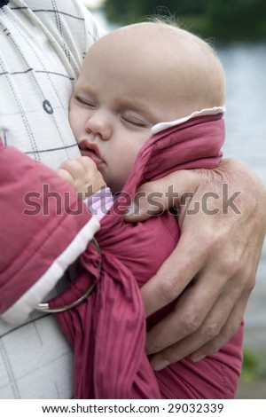 little cute girl sleeping in sling. Father`s hand hold her.  Summer time