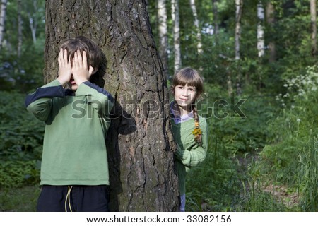 little boy close his eyes by hands. His friend look out tree. Hide-and-seek