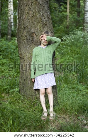 serious little girl close her eyes by hand  standing at big tree in forest