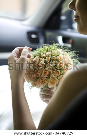 bride sitting on car hold bouquet of rose