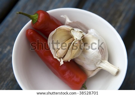 Garlic and traffic light chili pepper in a small round white bowl on blue wooden old table