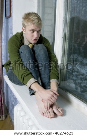 young handsome blond man in green sweater sitting on window-sill