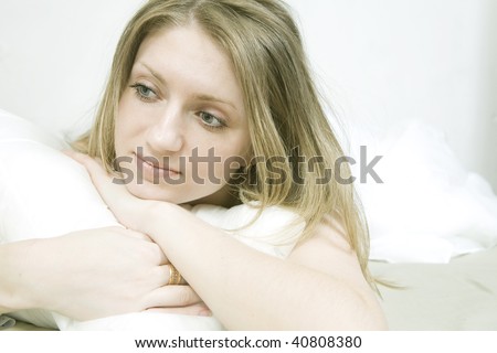 Young bored woman with lying down ot he bed over white background. Woman`s problem