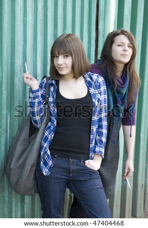 two smoking girls standing at the fence