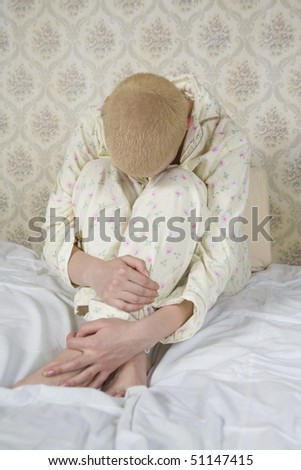 sad bald blond woman hugs her knees