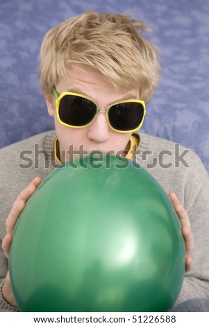 young blond man blowing a green balloon