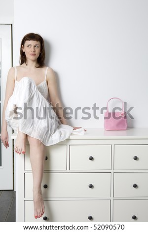 smiling flirting woman wearing white dress sitting on chest of drawers
