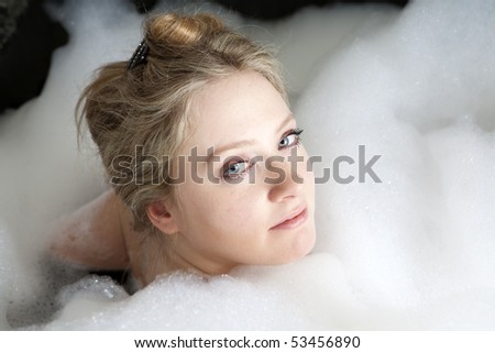 Young serious woman enjoys the bath-foam in the bathtub.