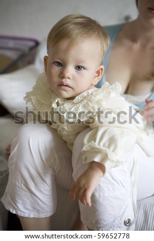 little cute baby wearing white dress sitting on mother`s knees