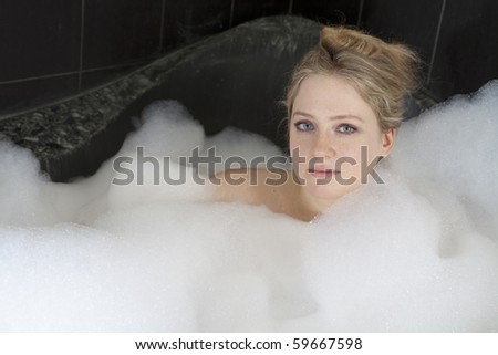 Young serious woman enjoys the bath-foam in the bathtub.