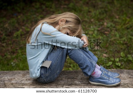 Unhappy little girl sitting on bench in park on autumn