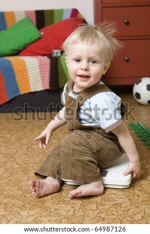 Boy measures weight on the floor scales. Boy sit down at floor scales on hardwood floor in living room.