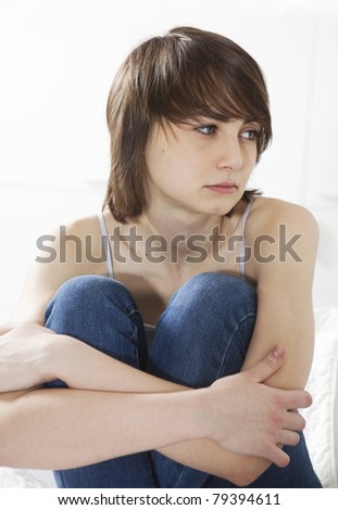sad girl sitting on the bed hugging her knees