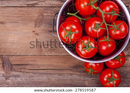 Tomatoes in and out of colander shot from above on wooden background