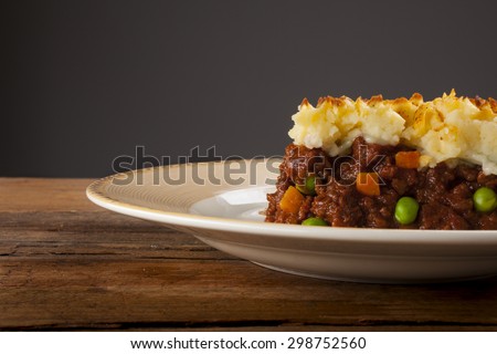 Shepherds pie shot front on on wood with grey background cropped close-up with negative space