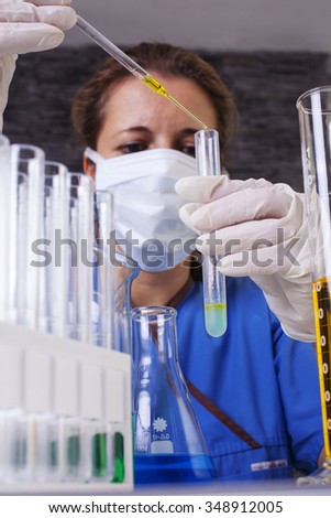 lab technician in scrubs and mask holding pipette and test tube shot front on on a dark  background portrait