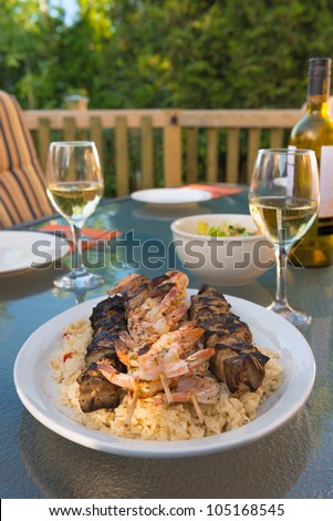 Outdoor meal with chicken and shrimp brochette on the rice. Alcohol white wine. Very shallow depth of field.