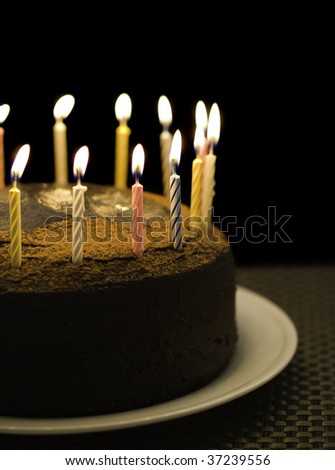 birthday chocolate cake with burning candle on the top. Black background and shallow depth of field.