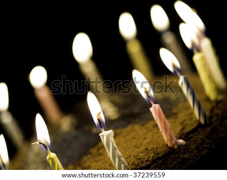 birthday chocolate cake with burning candle on the top. Black background and shallow depth of field.