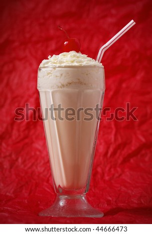 vanilla milkshake with whipped cream and cherry on the top. Focus on the cherry. Red background.