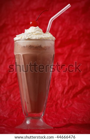 chocolate milkshake with whipped cream and cherry on the top. Focus on the cherry. Red background.