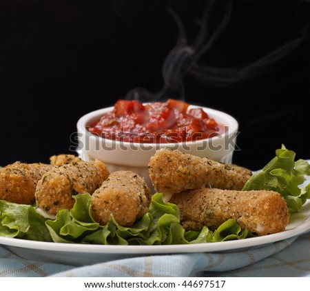 cheese sticks appetizer on salad with very hot salsa sauce. Smoke on the salsa with a black background.