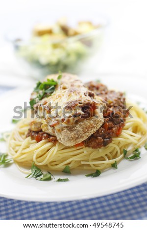 chicken parmigiana meal on a spaghetti with tomato and meat sauce. Caesar salad in the background.Shallow depth of field.