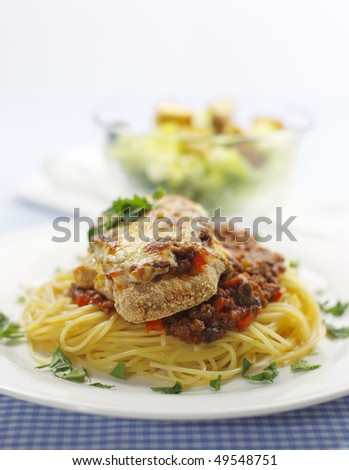 chicken parmigiana meal on a spaghetti with tomato and meat sauce. Caesar salad in the background.Shallow depth of field.