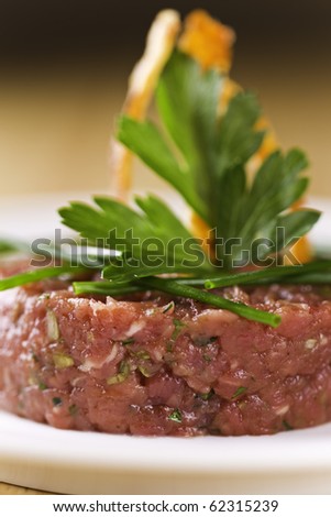 Loin beef tartar on a white plate with parsley on the top. Very shallow depth of field.Focus on the front of the meat.