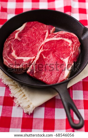 Two beautiful pieces of raw beef meat in a black iron frying pan. Shallow depth of field and red background.