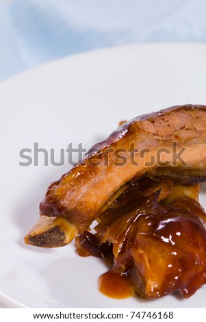 Pork meat spare rib with barbecue sauce on it. White plate with blue background and space to ad your text.