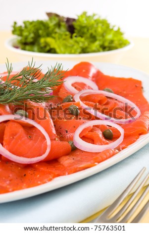 Appetizer smoked salmon with caper, spice and salad in the background. Very shallow depth of field.