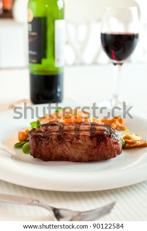 Surf and turf meal with fresh scampi and steak. Red wine in the background and shallow depth of field.