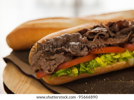 Beef sandwich with tomato and salad on a table. Very shallow depth of field.