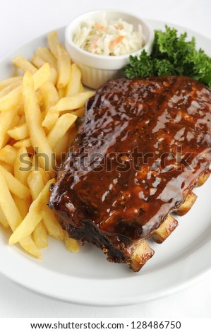 Grilled juicy barbecue pork ribs in a white plate with fries, coleslaw and parsley.
