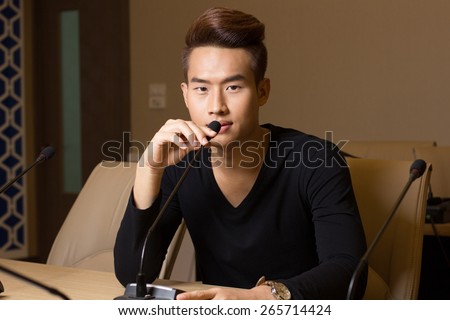 a portrait a man sit on the chair with microphone  on the table