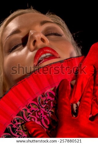 Beautiful woman in red sexy dress with fan. On black background.