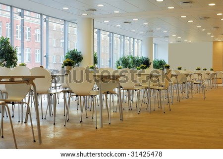 An empty cafeteria interior shot. Large windows letting in light.