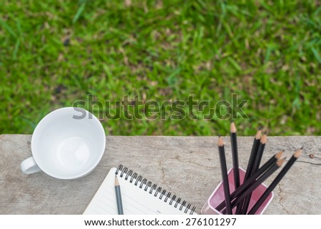 cup  notebook pencils on wooden table and grass in garden