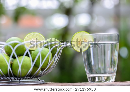 Lime in steel basket and glass of lime juice on a wooden table.