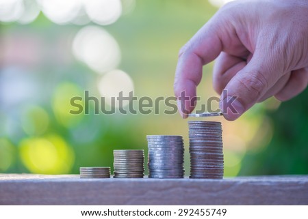 hand putting coin in increasing stack of money coins, saving money.