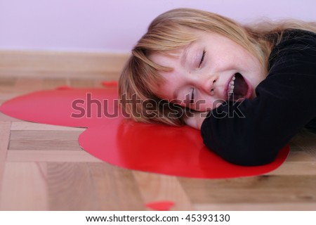 Pretty little girl yawning while laying on big red paper heart, dreaming about big love