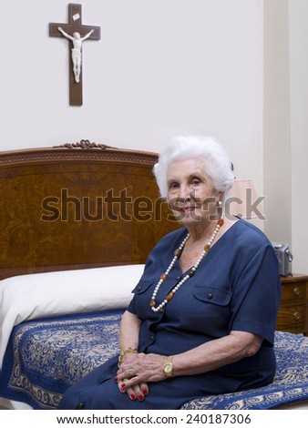 Portrait of an elderly woman sitting on her bed, looking at the camera